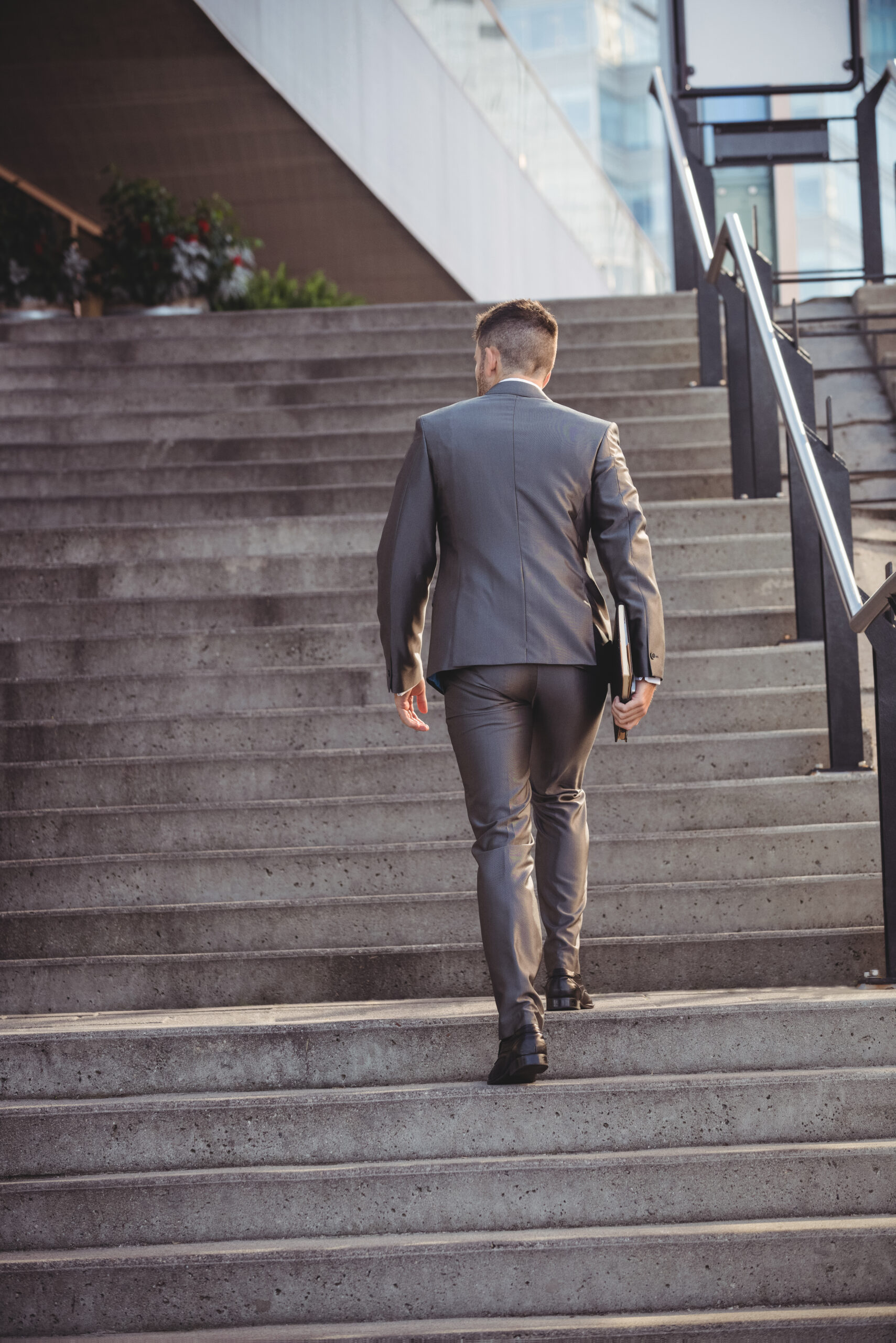 Rear view of businessman with a diary climbs up stairs in office